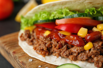 Delicious tortilla with meat and vegetables on wooden board, closeup view