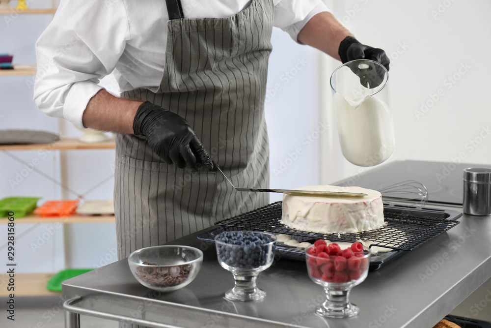 Wall mural male pastry chef preparing cake at table in kitchen, closeup