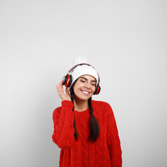 Young woman listening to music with headphones on grey background