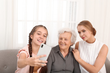 Happy sisters taking selfie with their grandmother at home