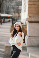 Elegant girl walk in a winter city. Woman in a white knited sweater. Beautiful lady with dark hair.