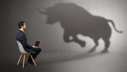 Humble businessman staying and offering stuffs to a huge angry bull shadow