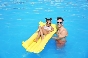 Little girl on inflatable mattress with father in swimming pool