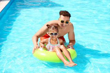 Happy father and little daughter with inflatable ring in swimming pool
