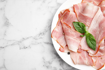 Plate of sliced raw bacon on white marble table, top view. Space for text