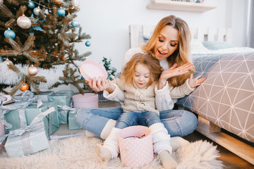 mother and beautiful blonde baby girl opening presents next to the christmas tree