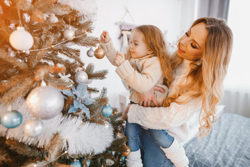 blonde mother and daughter decorating the christmas tree by hanging ornaments before the holidays