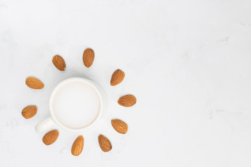 Almond milk with almonds around in sun shape, white concrete background. Non-dairy, vegan concept. Top view, flat lay, copy space