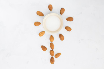 Almond milk with nuts around in flower shape, white concrete background. Non-dairy, vegan concept. Top view, flat lay, copy space