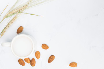 Almond milk in cup, nuts, plant on white concrete background. Non-dairy, vegan concept. Top view, flat lay, copy space