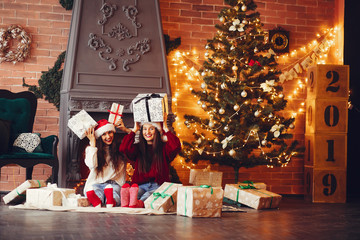 Two pretty girls sitting near Christmas tree. Beautiful ladies in a studio