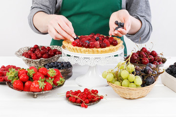 Woman decorates a big tart with variety of fruits.