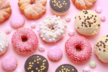 Various types of donuts and other cakes on pink background.