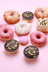 Various types of donuts and other cakes on pink background.