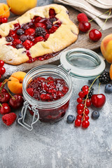 Jar of cherry jam among fresh fruits on grey stone background.