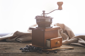 coffe bean with grinder and coffee in wooden spoon on wood table in morning light.