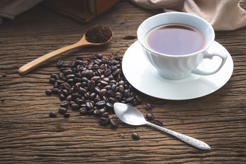 A cup of hot coffee with wooden spoon  and cofee bean on wooden table in morning light.