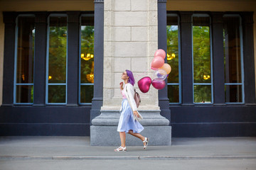 Girl with purple hair walking outdoor with bunch of helium baloons