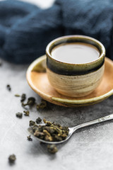 A cup of hot green tea with dry leaves in spoon on cement table. Healthy drink concept.