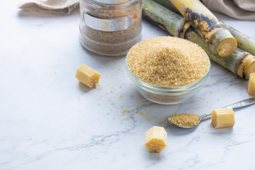 Brown sugar in bowl with spoon and sugar cane on wooden table.