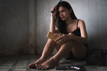 Low key portrait of young Asian woman is holding knife and drugs in the old room. Social problems, crime and drugs concept.