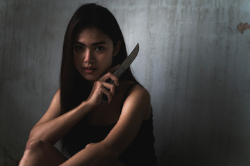 Low key portrait of beautiful Asian woman is holding knife in the old room. Social problems, crime and drugs concept.