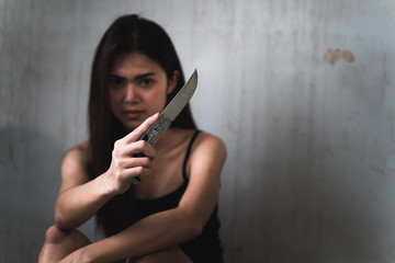Low key portrait of beautiful Asian woman is holding knife in the old room. Social problems, crime and drugs concept.