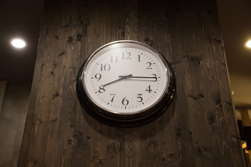black and white steel clock decorate on dark wooden wall in kitchen. perspective angle clock wall.