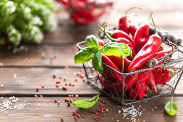Red chili peppers with a sprig of basil in a wicker metal basket on a wooden background.