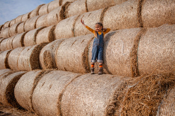 Cute girl having fun on rolls of hay bales in field