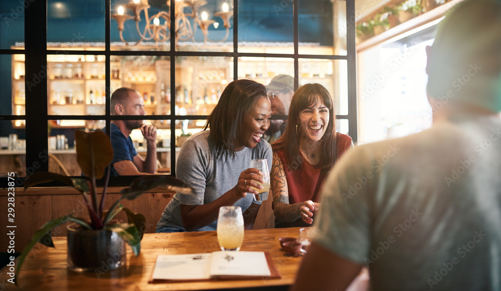 Wall mural Diverse young friends laughing over drinks together in a bar