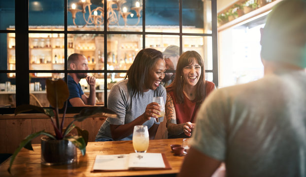Diverse young friends laughing over drinks together in a bar