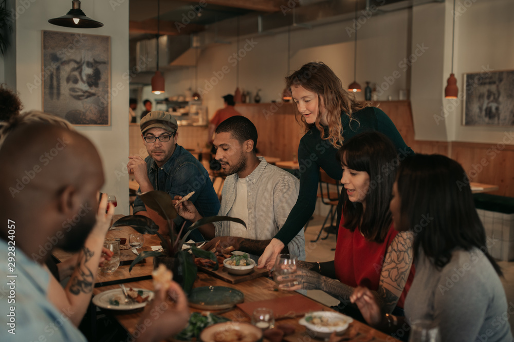 Wall mural Waitress delivering food orders to a table of smiling customers