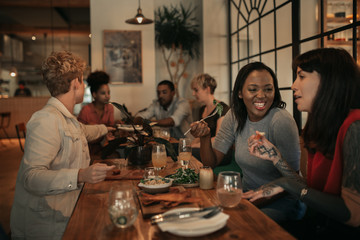 Smiling friends sharing food while sitting at a bistro table