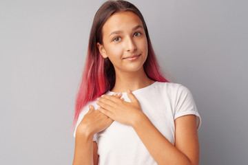 Young teen girl touching her heart with her hands over gray background.