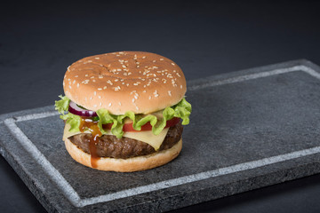 Hamburger with a double serving of meat, tomatoes, salad, onions on a wooden board in a restaurant.Copy space