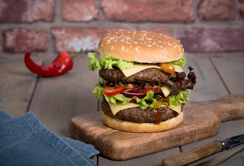 Hamburger with a double serving of meat, tomatoes, salad, onions on a wooden board in a restaurant.Copy space