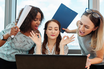 Pretty young Asian businesswoman sitting at desk with opened laptop and trying to stay calm and...