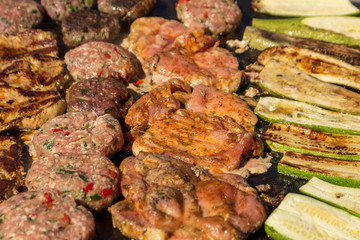 Meat grilled pork with vegetables. Meat balls and steak during grilling. Close up.