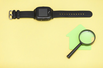 Flat lay of kids smart watch with magnifying glass on yellow background. Concept of navigation and venue. Find child, determine location. Copy space.