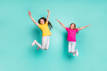 Fototapeta na wymiar Full length body size photo of two enjoying girls being free wearing yellow and pink t-shirts while isolated with teal background
