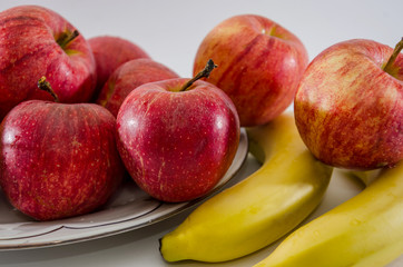 red apples and bananas in a plate isolated on white background. Close-up.