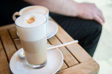 Glas Latte Macchiato und Tasse Cappuccino Kaffee mit Milchschaum auf Holztisch draußen im Straßencafé 