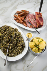 Oldenburger Grünkohl, Kassler Nacken, Kohlwurst und Pinkel auf Platten mit Kartoffeln und Senf auf Marmor Tisch