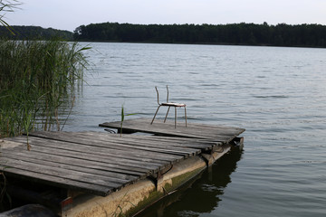 Fototapeta premium A broken chair is on an old wooden pier on the shore of a fresh water lake.