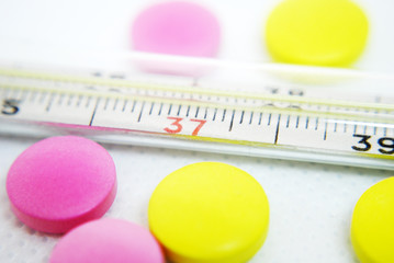  The thermometer and multi-colored pills on a white background