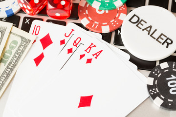 Online poker casino theme. Gambling chips with dice,playing cards, american dollars and dealer chip on laptop.