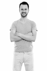 Studio shot of happy young man smiling and standing with arms crossed