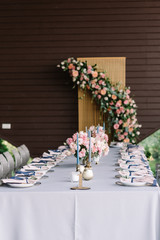 Long rectangular wedding table decorated with blue tablecloth, candles, luxurious flowers.