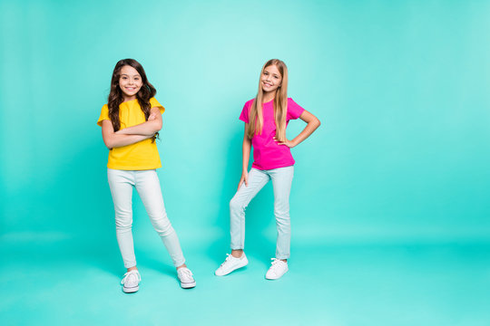 Full length body size photo of two young models posing in front of camera wearing pink and yellow t-shirts while isolated with turquoise background